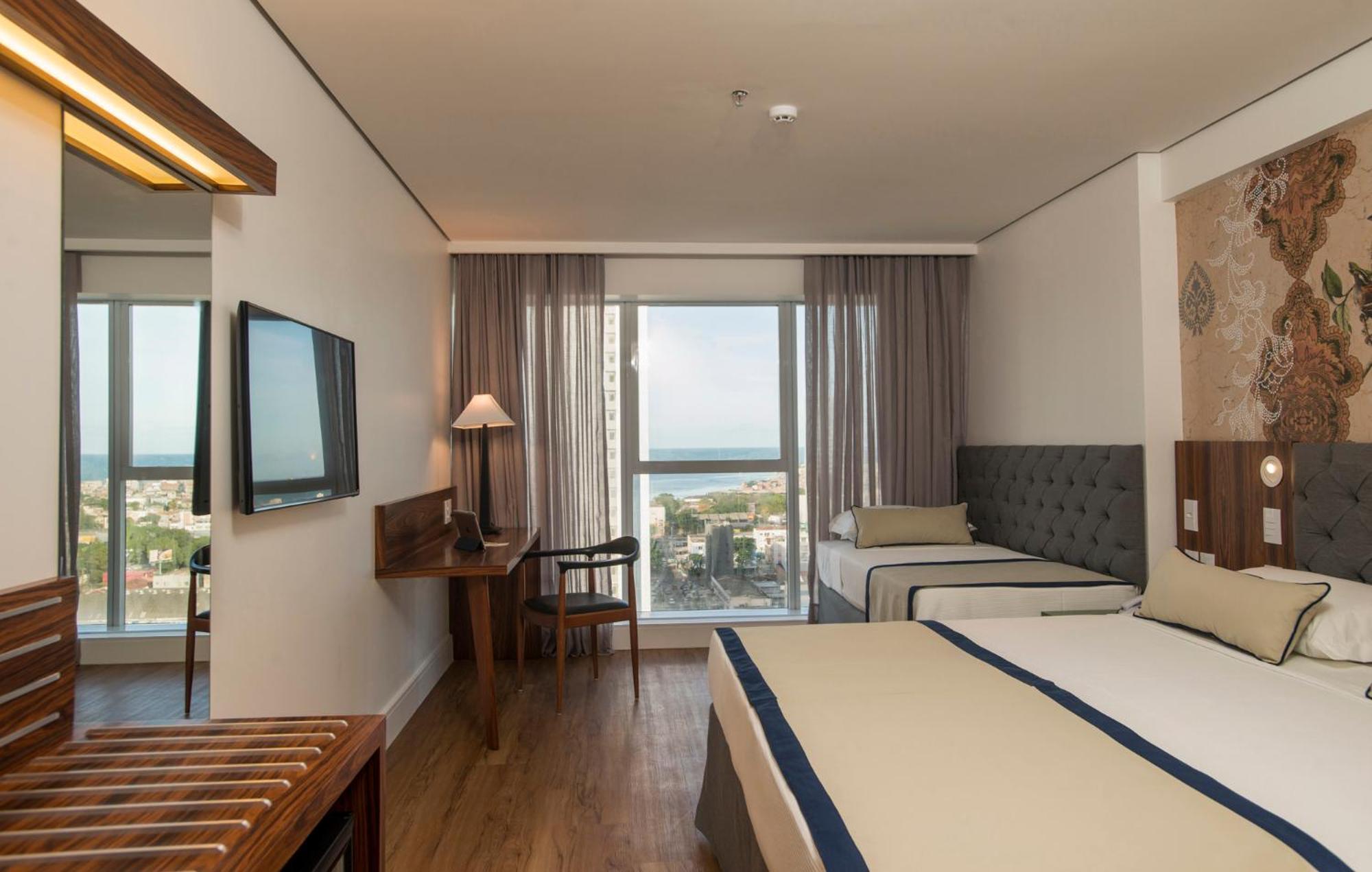 Hotel Luzeiros Recife Exteriér fotografie The photo shows a hotel room that features a modern and comfortable design. There are two beds: one larger bed and a smaller twin bed. The room has large windows with curtains that allow natural light to enter, offering a view of the outside, possibl